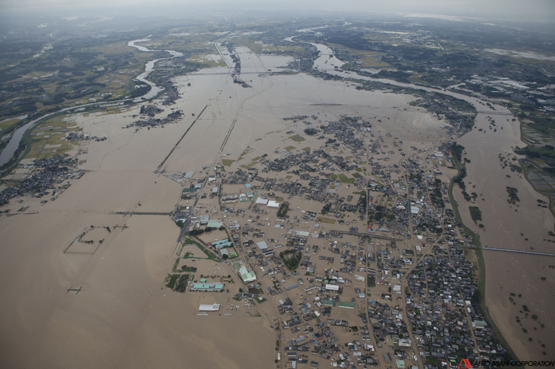 【常総市石下下流左岸　破堤箇所全景　上流側より】画面右中央が破堤箇所。手前が上流で奥が下流。左は東側を並行する小貝川で、水の色が全く異っている。氾濫浸水域は、この時点で下流側へ破堤箇所から約5.5kmまで達している。